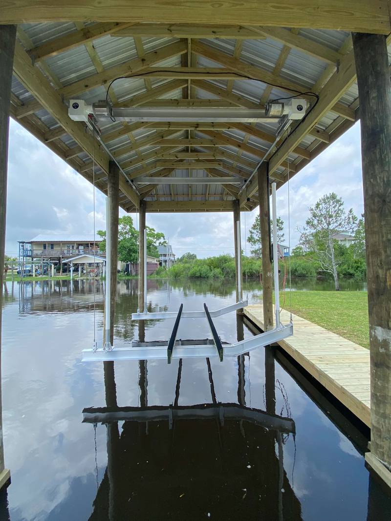 Inside a boathouse looking out, angled roof beams over the lift