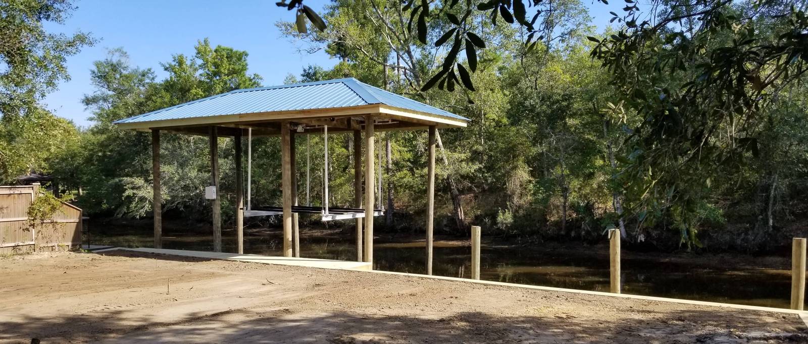 Open boathouse with a tin roof on a wooded shore