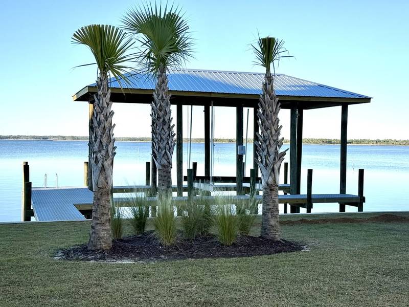 Boathouse with a dark roof behind palm trees and a lawn