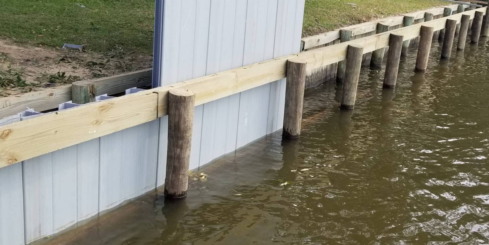 Flat-panel vinyl bulkhead with a wood cap and pilings along the water